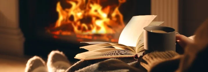 Person mit Tasse und Buch am Kamin